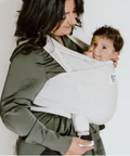 Woman holding a baby in a white sling against a plain background