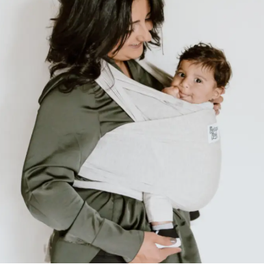 Woman holding a baby in a white sling against a plain background