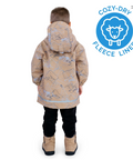 Child wearing a beige coat with animal pattern, standing against a white background, with Cozy-Dry logo on the right.