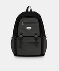 A dark gray and black backpack with multiple zippered pockets and a small white shield-shaped logo patch on the front, shown against a light gray background.