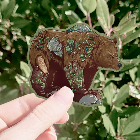 Hand holding a bear sticker with nature-themed design against a green leafy background