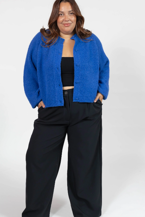 Person wearing a blue cardigan over a black top and pants on a white background