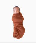 Newborn baby swaddled in a rust-colored blanket on a white background