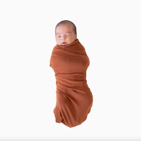 Newborn baby swaddled in a rust-colored blanket on a white background