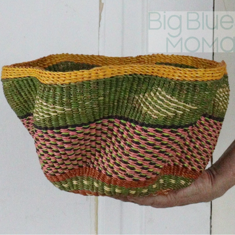 Handwoven basket with green, pink, and yellow pattern held by a hand against a white background.