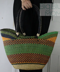 Woven bag with green and orange stripes held by a person against a plain background
