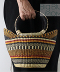 Woven handbag with striped pattern held by a person against a white background