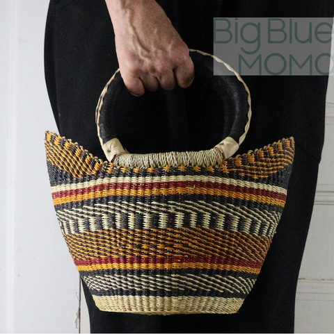Woven handbag with striped pattern held by a person against a white background