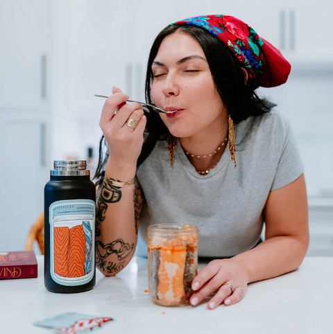 Woman eating from a jar with a bottle and book on a table