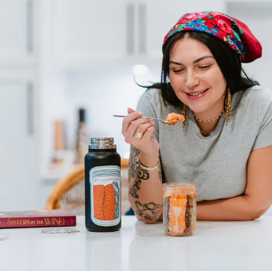 Woman eating from a jar with a bottle and book on a kitchen counter