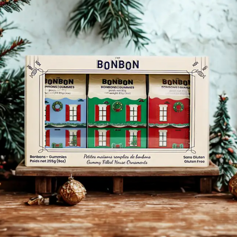 Box of BonBon gummy filled house ornaments with Christmas trees and decorations in the background