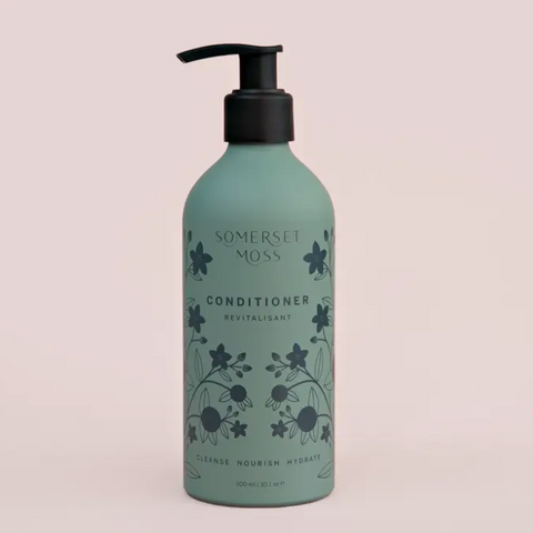 Green conditioner bottle with floral design on a light pink background