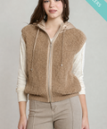 A woman models a brown fuzzy zip-up hooded vest over a cream ribbed long-sleeve top and beige pants against a light gray studio background. A teal 'BEST SELLERS' banner is in the top-right corner.