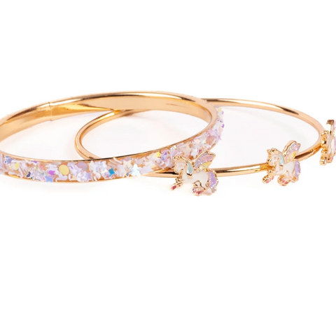 A pair of gold bangle bracelets, one adorned with a row of iridescent clear crystals and the other decorated with two matching crystal flower charms, set against a plain white background.