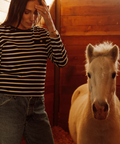 Woman standing next to a small white horse in a wooden stable.