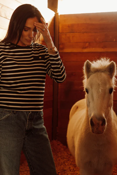 Woman standing next to a small white horse in a wooden stable.
