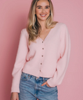 Woman wearing a pink cardigan and blue jeans against a pink background