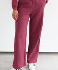 Person wearing a maroon tracksuit with white sneakers on a light gray floor and white wall background
