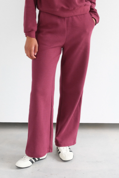 Person wearing a maroon tracksuit with white sneakers on a light gray floor and white wall background