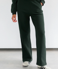 Person wearing dark green pants and white sneakers on a plain background
