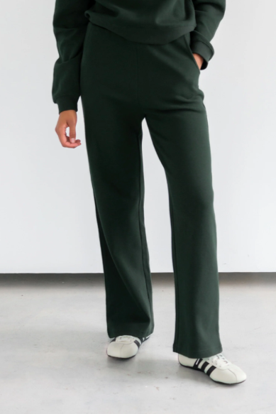 Person wearing dark green pants and white sneakers on a plain background