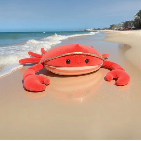 Plush crab toy on a sandy beach with ocean waves in the background