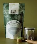 Tea package labeled 'Green Jasmine' with a tea scoop and strainer on a green background