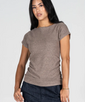 A woman modeling a short-sleeve crew-neck knit top in taupe brown, paired with dark denim pants, against a plain light gray studio background.