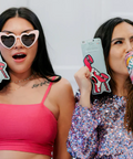 Two women holding colorful phone cases and a drink, with a neutral background