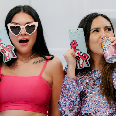 Two women holding colorful phone cases and a drink, with a neutral background