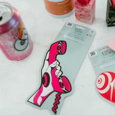 Pink and white phone-shaped product with sunglasses and other items on a white surface