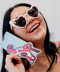 Woman wearing heart-shaped sunglasses holding a colorful card with a cartoon character.