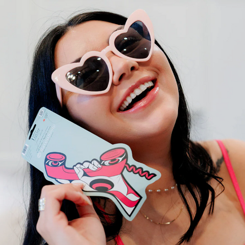 Woman wearing heart-shaped sunglasses holding a colorful card with a cartoon character.