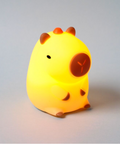 A cute, glowing yellow capybara night light with brown accents, photographed on a neutral gray background.