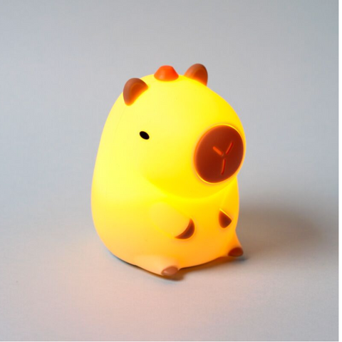 A cute, glowing yellow capybara night light with brown accents, photographed on a neutral gray background.