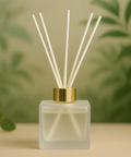 Reed diffuser with a gold cap on a blurred green leaf background