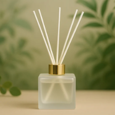 Reed diffuser with a gold cap on a blurred green leaf background