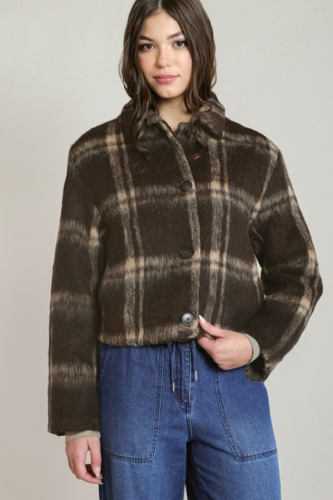 A woman modeling a cropped brown plaid jacket with a fuzzy texture, paired with blue jeans, against a plain light gray studio background.