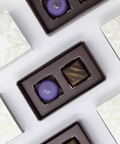 Assorted chocolates in brown boxes on a white surface with a decorative pattern.