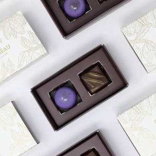 Assorted chocolates in brown boxes on a white surface with a decorative pattern.