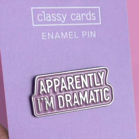 Enamel pin with 'Apparently I'm Dramatic' text on a purple card with 'classy cards' branding.
