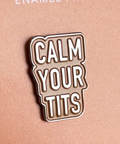 Enamel pin with 'CALM YOUR TITS' text on a pink background