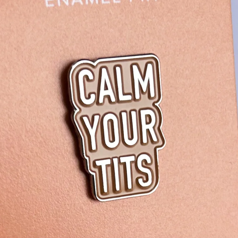 Enamel pin with 'CALM YOUR TITS' text on a pink background