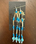 Pair of gold and turquoise beaded earrings on a display card against a wooden background