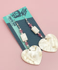 Shell earrings on a card with 'Coastal Hero Collective' branding on a wooden surface.