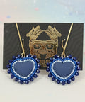 Blue heart-shaped earrings on a card with a gold design, placed on a wooden surface.