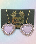 Heart-shaped earrings with pearl details on a dark card against a wooden surface