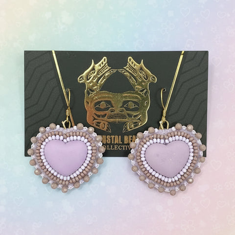 Heart-shaped earrings with pearl details on a dark card against a wooden surface