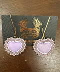Heart-shaped earrings with pearl details on a dark card against a wooden surface