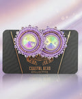 Decorative earrings on a black card with visible brand name, placed on a wooden surface.